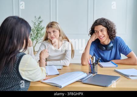 Smiling teenage students listening to female teacher Stock Photo