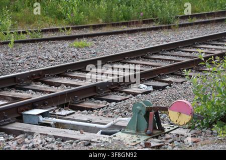 Close-up of a vintage manual railroad switch indicator mechanism with yellow and red weight on wooden ties and gravel track bed. Stock Photo