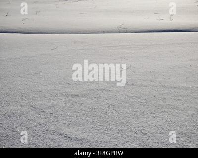 Snow blankets the ground with a soft surface and smooth patterns while the sun shines over the winter landscape in daylight. Stock Photo