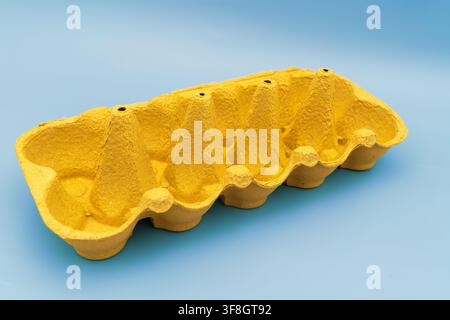 The image shows an empty yellow egg carton placed on a blue background. The carton has a unique shape with six sections for holding eggs. It is easy t Stock Photo