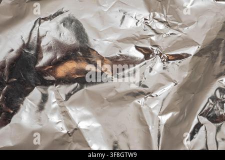 A piece of metal foil is crumpled on a flat surface. The surface reflects light, creating unique textures and patterns. This shows the details of the Stock Photo
