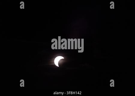 Riga, Latvia - August 12, 2026: Partial solar eclipse with crescent sun shining through dark clouds during a dramatic celestial event. Stock Photo