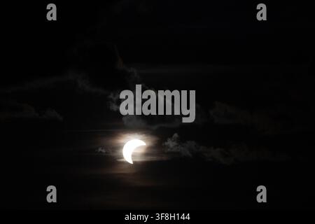 Riga, Latvia - August 12, 2026: Partial solar eclipse with crescent sun shining through dark clouds during a dramatic celestial event. Stock Photo