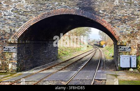 View through a stone arch bridge at Carrog station showing curved tracks and warning signs on the Llangollen Railway in Wales, UK. Stock Photo