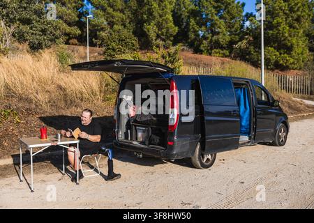 Amputee man enjoying van life outdoors reading book Stock Photo