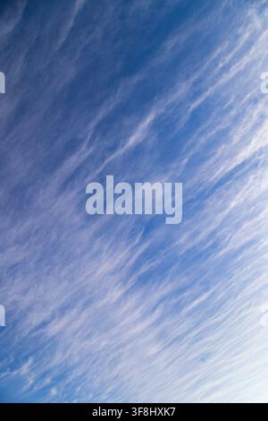 Delicate white cirrus clouds stretch diagonally across a vibrant blue sky. The soft, diffused lighting suggests a serene daytime atmosphere, creating Stock Photo
