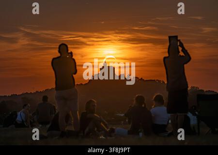 Crowd of people gathered on meadow watching partial solar eclipse over Kuneticka hora Castle during sunset in Pardubice, Czech Republic. Stock Photo