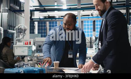 Technicians business people examining solar panel production in high tech facility, reflecting teamwork, efficiency and insight in the industrial production of alternative energy. Camera A. Stock Photo