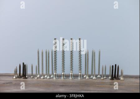 A stunning display of various screws lined up meticulously on a rustic wooden surface. Each screw varies in size and color, highlighting the diversity Stock Photo