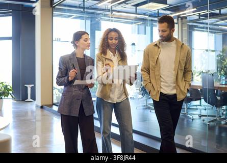 Three colleagues walking in modern office, discussing documents and planning Stock Photo