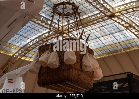 VIENNA, AUSTRIA, 7 February 2023: A wicker hot air balloon basket with hanging sandbags is suspended indoors beneath a large glass and metal roof near Stock Photo