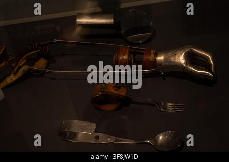 VIENNA, AUSTRIA, 7 February 2023: A historic prosthetic arm with attached adaptive eating utensils is exhibited in a dark museum display case. Stock Photo