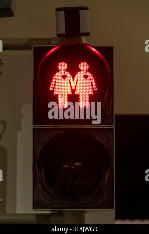 A red pedestrian crossing signal displays two illuminated female figures holding hands against a dark background. Stock Photo