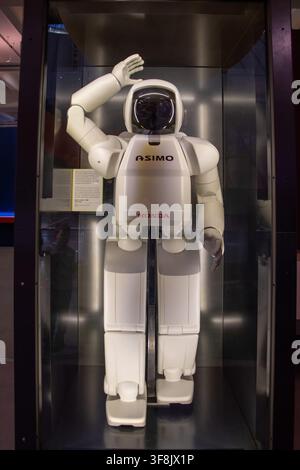 Honda ASIMO humanoid robot stands with a raised hand inside a glass display case. Stock Photo
