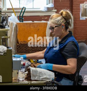 Tampa, FL, USA. 12th Aug 2026. An operator feeds tobacco wrapper leaf into a vintage cigar-making machine as a bin of freshly made cigars fills beside her in the machine-rolling area of J.C. Newman Cigar Co.'s El Reloj factory in Ybor City. The company still produces cigars on antique machines dating to the 1930s. Founded in 1895, fourth-generation J.C. Newman is America's oldest family-owned premium cigar maker, and the 1910 building - part of a National Historic Landmark District - is the last operating historic cigar factory in the US. Credit: Tosh Persons / Ģ����ý Live News Stock Photo