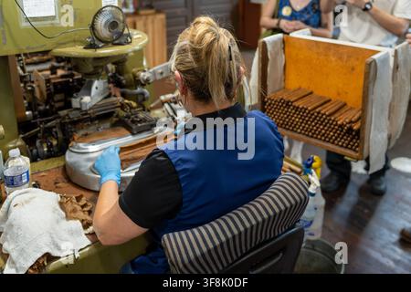 Tampa, FL, USA. 12th Aug 2026. An operator works wrapper leaf at an antique cigar-making machine as visitors on a factory tour pause beside a rack of freshly made cigars in the machine-rolling area of J.C. Newman Cigar Co.'s El Reloj factory in Ybor City. The company offers weekday tours of the 1910 clock-tower building, part of a National Historic Landmark District and the last operating historic cigar factory in the US. Founded in 1895, fourth-generation J.C. Newman is America's oldest family-owned premium cigar maker. Credit: Tosh Persons / Ģ����ý Live News Stock Photo