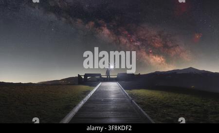 View of a person holding a bright light on a wooden walkway at Rifugio Belvedere under the Milky Way in Arquata del Tronto, Marche, Italy. Stock Photo