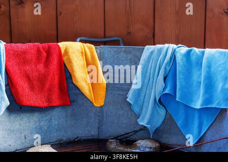 Colorful reusable microfiber cleaning cloths and towels draped over the rim of a galvanized metal tub Stock Photo