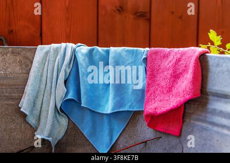 Colorful reusable microfiber cleaning cloths and towels draped over the rim of a galvanized metal tub Stock Photo
