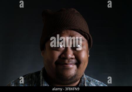 A close up portrait of a young Asian male from Indonesia Southeast Asia showing a happy and smiling facial expression against a dark background, The c Stock Photo