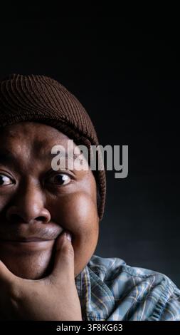 A close up portrait of a young Asian male from Indonesia Southeast Asia smiling with a finger on the chin against a dark background, The thinking man Stock Photo