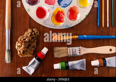 Art supplies laid out on a table: paint, brushes, palette, sponge Stock Photo