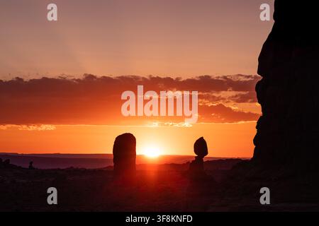 View of the sun setting behind desert rock formations in the landscape of Moab, Utah, United States. Stock Photo