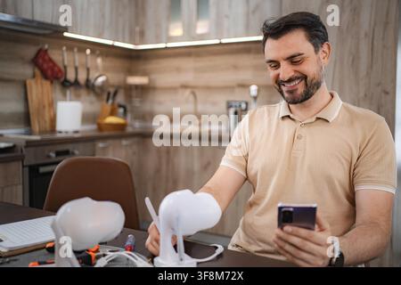 Male technician smiling and using smartphone while installing smart home devices in a kitchen Stock Photo