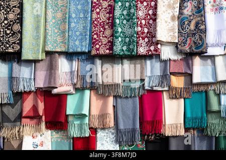 Colorful scarves and embroidered shawls displayed at Siab bazaar in Samarkand. Rows of folded textiles with fringe create a vibrant market scene ideal for travel and culture imagery. Stock Photo