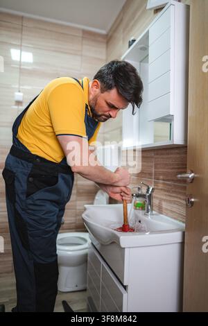 Plumber using plunger to unclog sink drain in bathroom Stock Photo