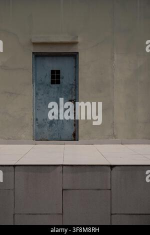 Old weathered metal door with lock on cracked concrete wall. Stock Photo