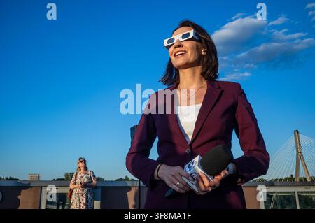 A television reporter seen looking at the sun through the filtered spectacles as the solar eclipse progresses. On the evening of the 12th August, Prime Minister of the Republic of Poland, Donald Tusk, joins scientific observers and members of the public at the Copernicus Science Centre in Warsaw to watch a partial solar eclipse. At its maximum, the Moon obscures about 82% of the Sun as viewed from the Polish capital. Warsaw's eclipse runs from approximately 19:14 until sunset at 20:06, reaching its maximum at 20:02. The roughly 82% figure refers to the Sun's covered area; the eclipse magnitude Stock Photo