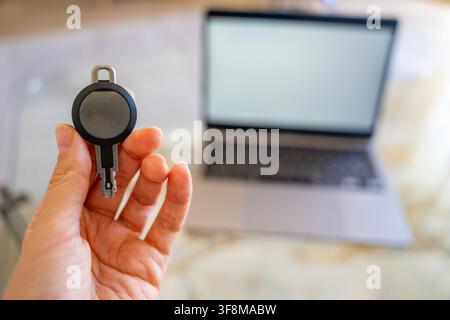 Hand holding an RFID key fob in front of a computer monitor. Concept of programming electronic access credentials, smart security systems and digital Stock Photo