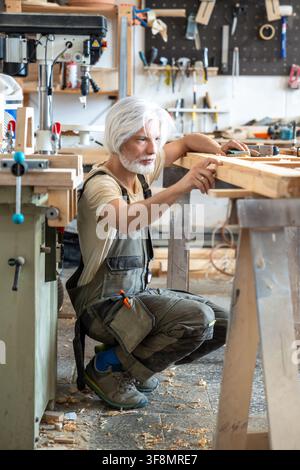 Passionate craftsman attentively checking surface of antique wooden door at worktable in workshop Stock Photo
