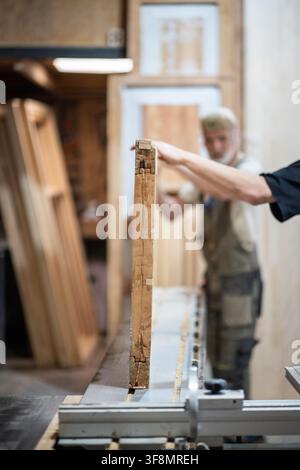 Professional woodworking studio working process, skillful carpenters placing vintage wooden door at workbench in woodshop, workflow in private repair Stock Photo