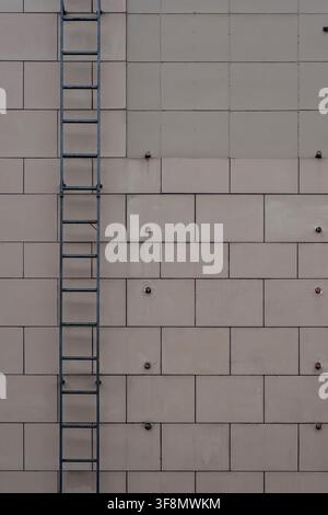 Building facade featuring beige rectangular cladding panels, exposed bolts, and a dark metal fire escape ladder. Stock Photo