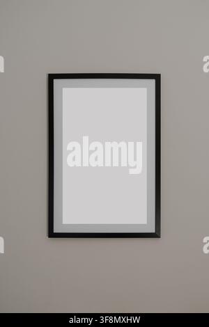 Blank vertical black picture frame mockup hanging on a simple gray wall. Stock Photo