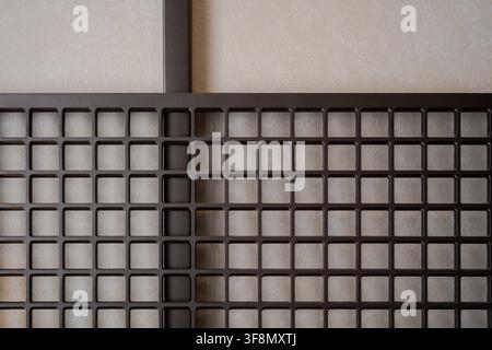 Dark metal grid partition screen against a light textured wall background. Stock Photo