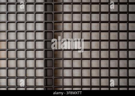 Abstract geometric pattern of a dark metal lattice screen over a textured beige wall. Stock Photo