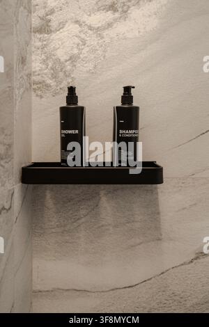 Black shower gel and shampoo dispenser bottles on a shelf in a modern marble bathroom. Stock Photo