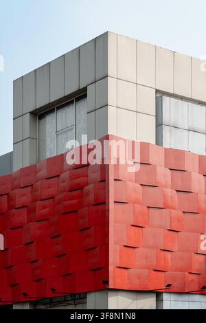 Modern building exterior featuring textured red facade and geometric gray panels against blue sky. Stock Photo