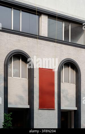 Blank red banner hanging on a modern brick building facade with arched windows. Stock Photo