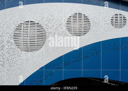 Modern architectural facade with perforated metal panels, curved blue and white design, and circular louvered vents. Stock Photo
