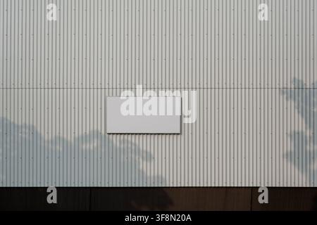 Blank white signboard on corrugated metal wall with tree leaf shadows. Stock Photo