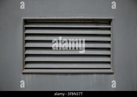 Extreme close up of a single rectangular slatted air ventilation grille on a painted grey metal surface. Stock Photo