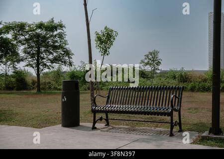 Black metal park bench and trash bin on concrete path. Stock Photo