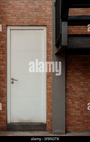 White closed door on a red brick wall near a concrete pillar and metal stairs. Stock Photo