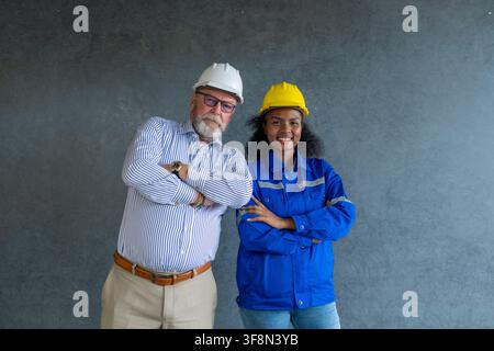 Engineer senior and woman engineer wearing safety helmets discussing blueprints in office collaborating on construction. Stock Photo
