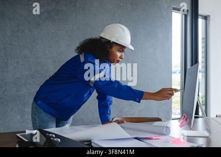 Portrait engineer wearing safety helmet and uniform standing gray background appears focused and professional representing. Stock Photo