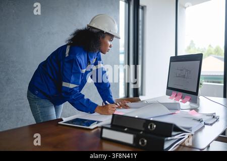 Portrait engineer wearing safety helmet and uniform standing gray background appears focused and professional representing. Stock Photo